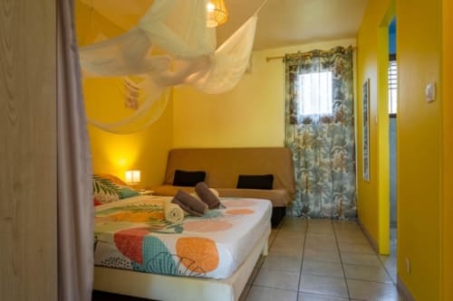 Bright yellow bedroom in Guadeloupe gîte with twin beds, sheer canopy, colorful bedding, and tropical décor