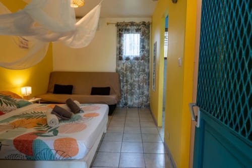 Bright yellow cottage bedroom at Gîtes Bagatelle in Guadeloupe with bed, seating area, and teal accents