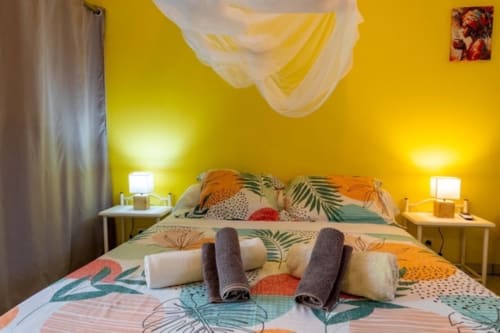 Bright yellow bedroom with tropical patterned bedding, rolled towels, and bedside lamps at Gîtes Bagatelle in Guadeloupe