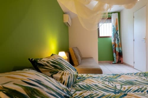 Bright bedroom with tropical-patterned bedding, green accent wall, and air conditioning at Gîtes Bagatelle, Guadeloupe