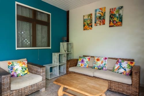 Colorful living room with rattan furniture, tropical pillows, and turquoise walls at Gîtes Bagatelle, Guadeloupe