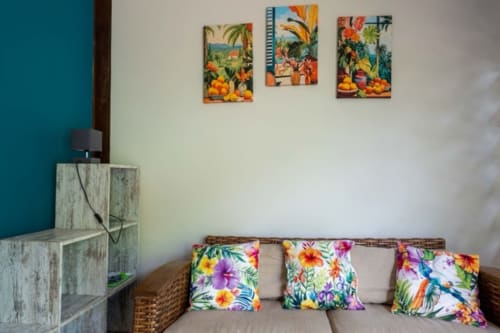 Cozy cottage living room in Sainte-Rose, Guadeloupe with colorful floral pillows, wicker sofa, and tropical wall art