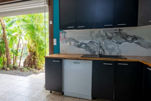 Modern equipped kitchen with black cabinets, mountain backsplash, and garden view at Gîtes Bagatelle, Guadeloupe