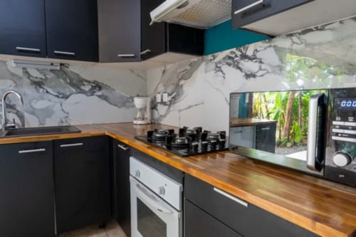 Modern kitchen in Guadeloupe cottage with marble backsplash, wood countertop, black cabinets, gas stove, and microwave.