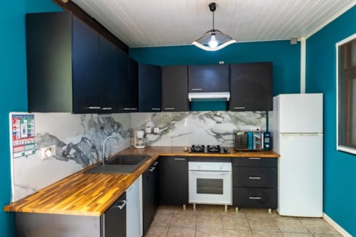 Modern equipped kitchen with turquoise walls, black cabinets, wooden countertops and marble backsplash in Gîtes Bagatelle