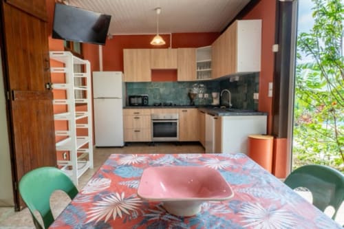 Modern cottage kitchen and dining area at Gîtes Bagatelle, Guadeloupe with equipped kitchen, orange accent walls and colorful
