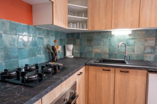 Modern equipped kitchen with turquoise tile backsplash, gas stove, sink, natural wood cabinets in Guadeloupe cottage