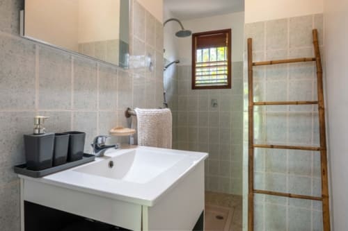 Modern bathroom with white sink, tiled walls, wooden towel ladder, and rain showerhead at Gîtes Bagatelle, Guadeloupe cottage