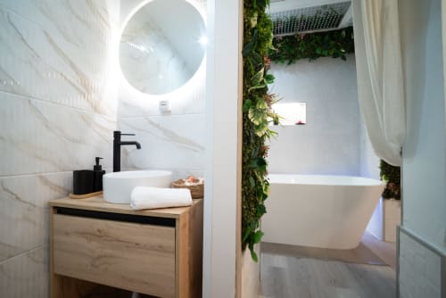 Baño moderno en apartamento Glow de Luxer Holidays Málaga con espejo redondo blanco, lavabo sobre encimera, bañera profunda y salón