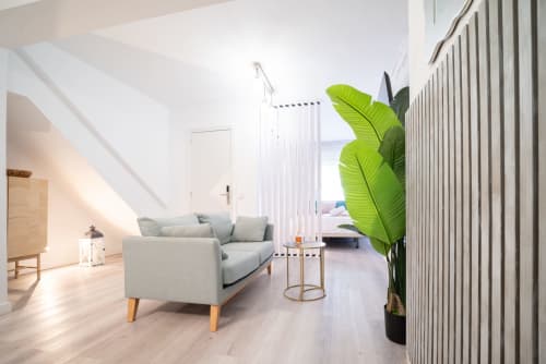 Luminoso apartamento moderno Glow en Luxer Holidays Málaga con sofá gris, suelo de madera y exuberante planta tropical