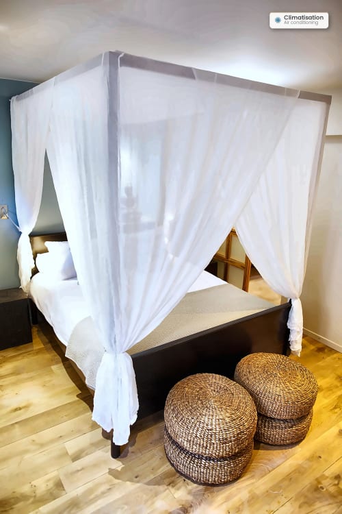 Elegant canopy bed with white curtains and woven poufs in Première Loge apartment at AJOUCADOU, Lourmarin