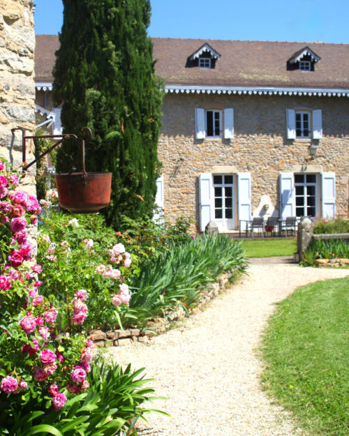Le Clos Ayanna, gîte de charme à Crémieu avec façade en pierre, volets bleus, roses roses et cyprès
