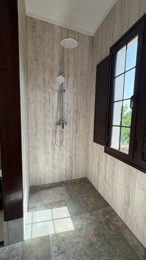 Modern shower at Villa Estrella Polar with rainfall showerhead, hand spray, and wood-grain tile walls in Tahiche, Lanzarote