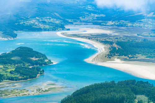 Vista aérea de laguna costera turquesa con playas de arena blanca y bosques cerca de Turismo Rural O Vilar en Galicia