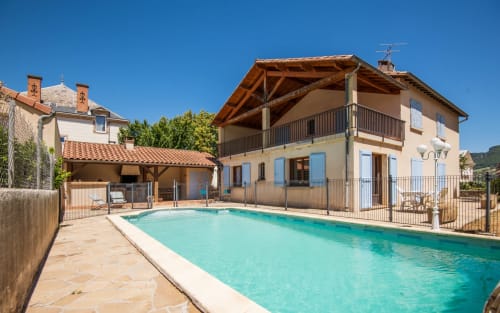 Millau villa with private turquoise pool, terrace, wooden pergola and manicured garden under clear blue sky
