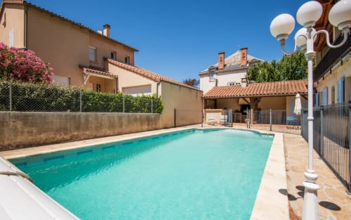 Private swimming pool with turquoise water at villa in Millau, France, surrounded by terracotta roofed buildings and