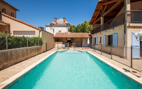Turquoise swimming pool with loungers, Mediterranean villa in Millau with terrace and surrounding buildings under clear blue