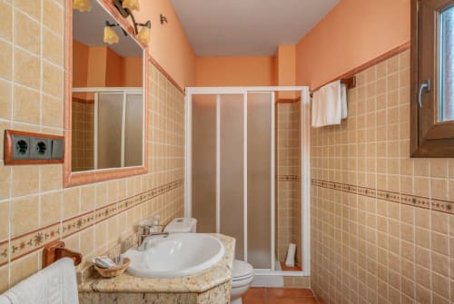 Modern bathroom in Hotel Balcón De Los Montés, Colmenar with beige tiles, white sink, shower, and orange accents