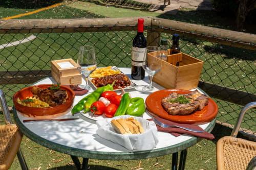Outdoor dining spread at Hotel Balcón De Los Montés with grilled meats, fresh vegetables, bread, and Spanish wine on a sunny