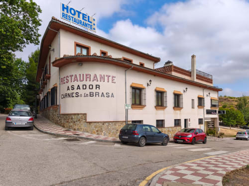 Hotel Balcón De Los Montés restaurant exterior in Colmenar with white building, parked cars, and blue sky