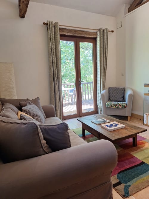 Séjour lumineux avec canapé marron, fauteuil crème, table en bois, tapis coloré et portes-fenêtres donnant sur le jardin