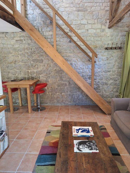 Intérieur rustique de chaumière en pierre avec escalier bois, tabouret rouge, table en bois et tapis coloré à La ferme de Roquedure