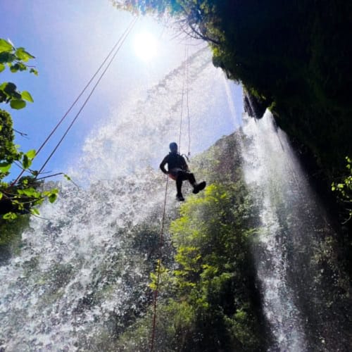 Persona descendiendo en rappel por una cascada rodeada de rocas cubiertas de musgo y vegetación exuberante cerca de Ròtova, España