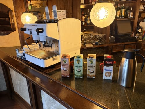 Barra de café del Hostal Juan Carlos en Carboneras con máquina espresso, bebidas vegetales y lámpara decorativa