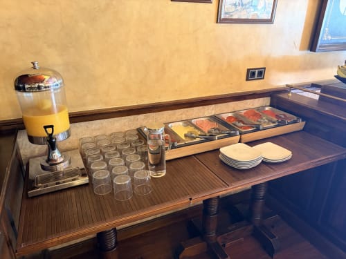 Desayuno buffet del Hostal Juan Carlos en Carboneras con dispensador de zumo, vasos, pastelería y platos sobre madera