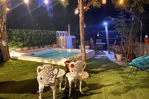Piscina del jardín al atardecer en la Cabaña La Vereda del Río Guadalquivir en Mogón, con sillas blancas ornamentales e iluminación ambiental