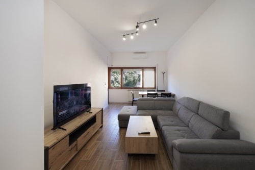 Soggiorno moderno dell'appartamento ViOletta a Lido di Ostia con divano grigio, mobile TV in legno e vista sul balcone
