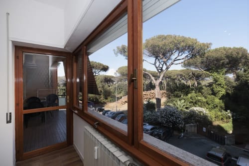 Balcone moderno dell'appartamento ViOletta Lido di Ostia con porte in legno, vista sui pini mediterranei e auto parcheggiate