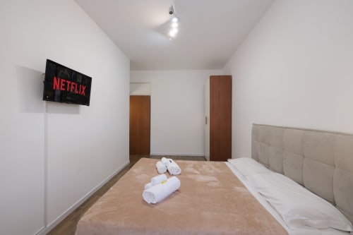 Camera moderna agli appartamenti ViOletta a Lido di Ostia con TV Netflix, letto beige, asciugamani bianchi e porte in legno