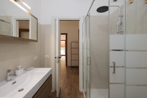 Bagno moderno nell'appartamento ViOletta a Lido di Ostia con lavabo bianco, ampio specchio e doccia walk-in