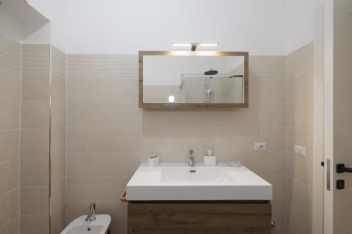 Bagno moderno dell'appartamento ViOletta a Lido di Ostia con lavabo bianco, mobile in legno e specchio incorniciato