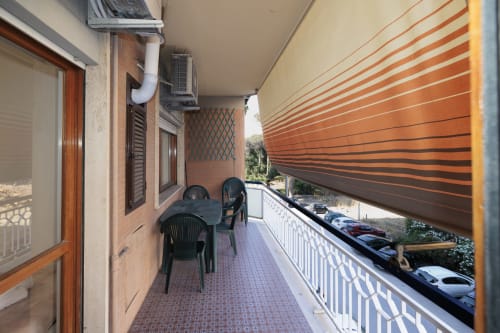 Balcone dell'appartamento ViOletta a Lido di Ostia con sedute, tenda a righe e vista sul parcheggio