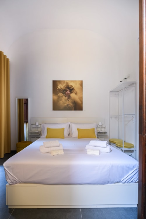 Camera da letto Ambra Almatros Design Suite con letto bianco, cuscini gialli e opere d'arte dorate a Sulmona