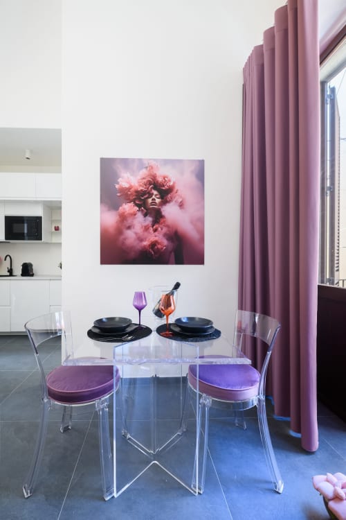 Moderna zona pranzo dell'appartamento Almatros Peonia a Sulmona con sedie trasparenti, cuscini rosa e ritratto artistico di nuvole