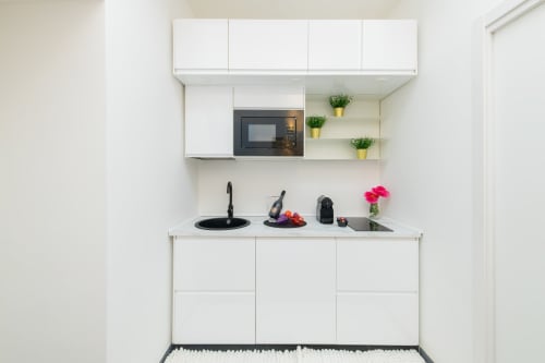 Moderna cucina bianca nell'appartamento Peonia di Almatros a Sulmona, con microonde, lavello e piante in vaso sugli scaffali