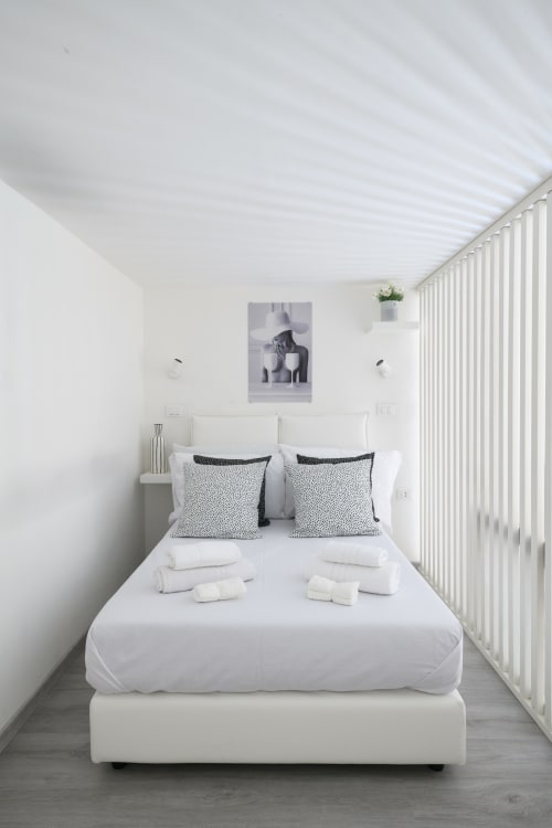 Camera da letto minimalista all'Almatros Design Suite di Sulmona con letto bianco, cuscini geometrici e persiane rigate