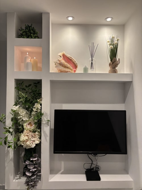 Modern wall-mounted TV in cottage with decorative shelves displaying plants, candles, and seashell décor at Domaine De Marly