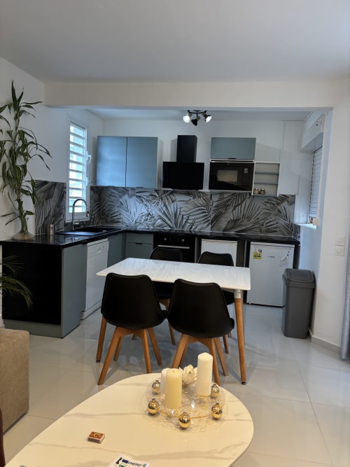 Modern kitchen-dining area at Domaine De Marly cottage with black appliances, tropical backsplash, and dining table with