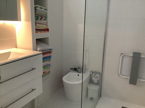 Salle de bains moderne de l'appartement Barcaresa au Barcarès : vasque blanche, toilettes, rangements pour serviettes et douche vitrée