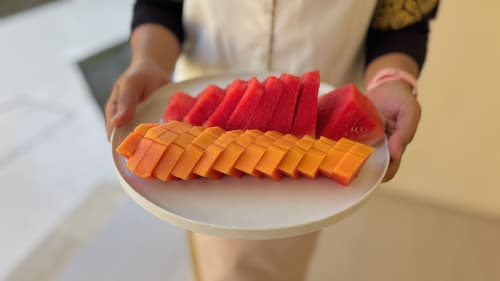 Person holding white plate with sliced red watermelon and orange papaya at Oasis Dune Villas, Lombok