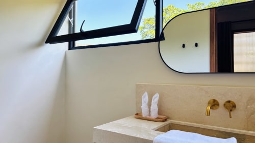 Modern bathroom sink with gold faucets and mirror at Oasis Dune Villas Lombok villa, featuring stone vanity and skylight
