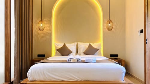 Luxury villa bedroom with glowing arched headboard, white bedding, gold pendant lights, and wooden accents at Oasis Dune