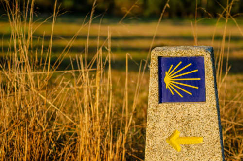 Señal del Camino de Santiago en poste de piedra en Galicia, orientando peregrinos cerca de un alojamiento rural en A Coruña