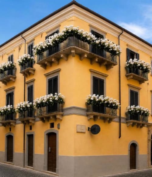 Luminoso edificio giallo dell'hotel Almatros a Sulmona con balconate fiorite bianche