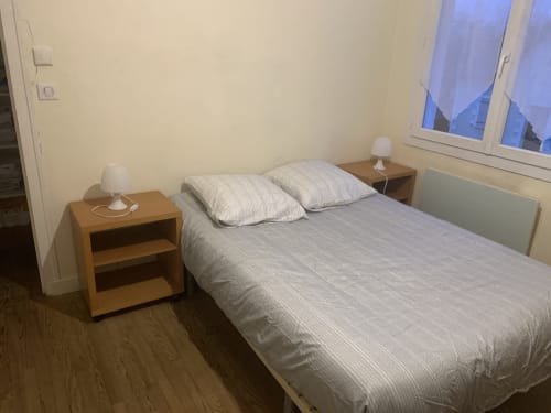 Chambre confortable à la Villa des Palmiers avec lit double, literie rayée, table de nuit en bois et vue sur le jardin