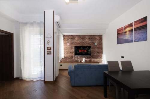 Modern apartment living area at ViOletta, Lido di Ostia with blue sofa, flat-screen TV, brick wall, dining table, and wooden